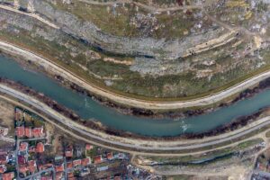 Фотографија од воздух од реката Вардар, на едната страна има дива депонија, а на другата страна населба со куќи.