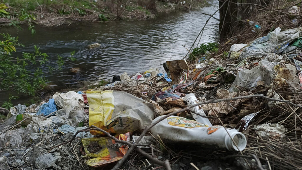 Фотографија на која се гледа ѓубре насобрано покрај река.
