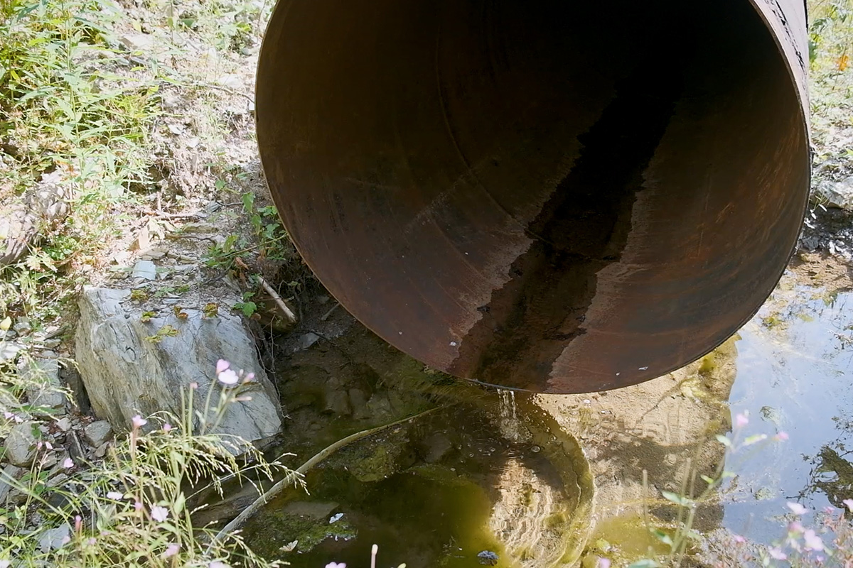 Слика од голема цевка низ која тече мала количина вода од мала хидроцентрала